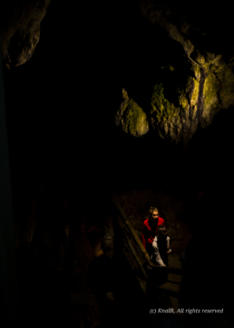 Femme habillée d'un pull rouge éclairée dans un escalier du Gouffre de Padirac